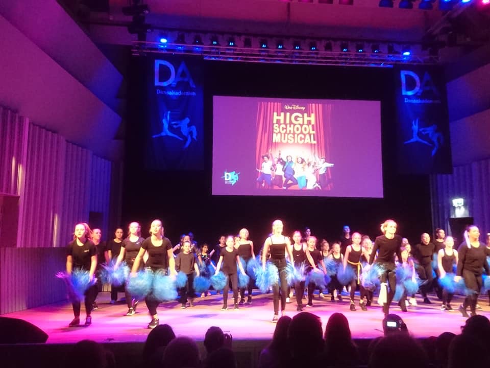 Dansare på scen i svarta kläder och blå pompoms